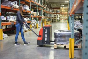 A woman pulls a pallet jack through a warehouse.