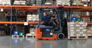 A forklift operator drives an electric forklift in a warehouse. 
