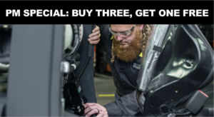 Bearded mechanic wearing safety glasses inspecting the interior of an open car door in a workshop.